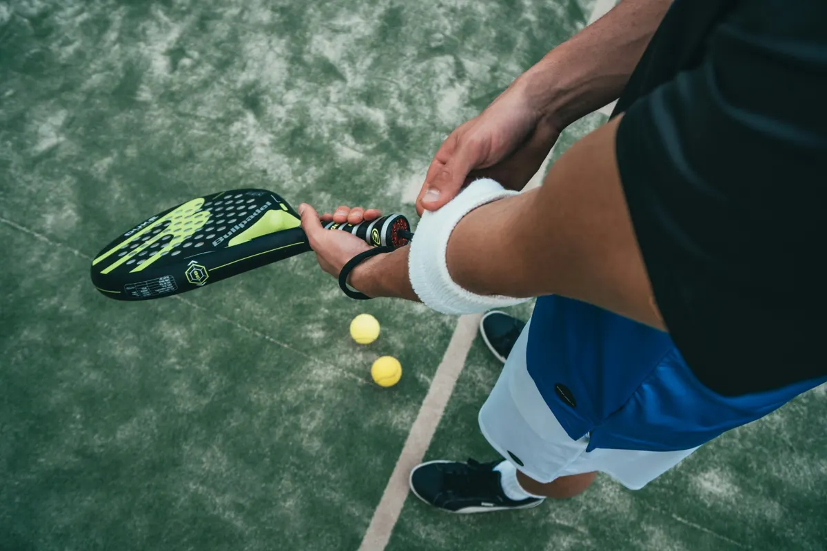 Player gripping a padel racket, two balls on the court